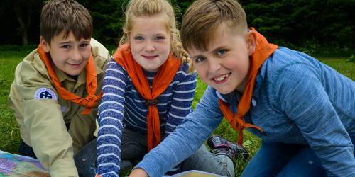 Drei Kinder mit orangenem Halstuch zeigen auf eine Weltkarte