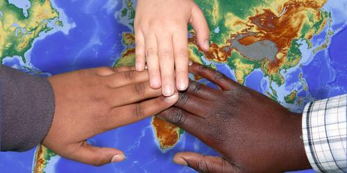 Drei Hände berühren sich auf einer Weltkarte