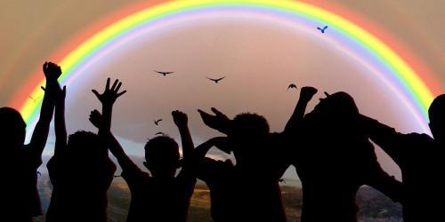 Vor einem Regenbogen zeichnen sich dunkle Silhouetten von Kindern ab