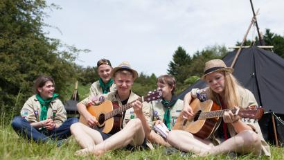 Eine Gruppe Jugendlicher sitzt mit Gitarre vor einem Zelt
