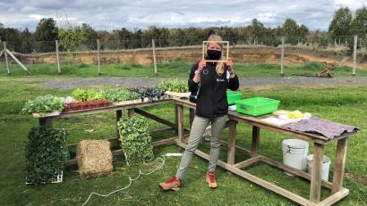 Workshop in der Natur: Tisch mit Pflanzensetzlingen, im Vordergrund Julia mit einem Holzrahmen in der Hand