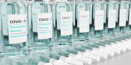 Nebeneinander stehende, durchsichtige Ampullen, auf denen Covid-Impfstoff steht.