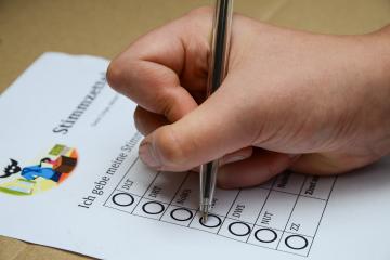 Eine Hand mit einem Stift auf einem Stimmzettel mit dem Kobold