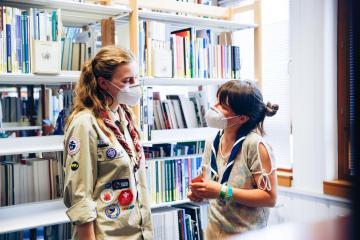 Zwei Pfadfinderinnen unterhalten sich in einer Bibliothek